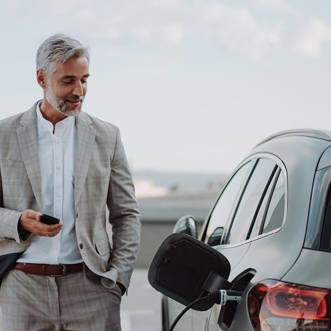 Well dressed gentleman standing next to electric car on phone